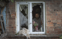A local resident places a vase with flowers on a broken window in his house damaged by the Russian shelling in Bakhmut, Donetsk region, Ukraine. June 26, 2022. AP Photo/Efrem Lukatsky.